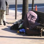 unhoused person laying on a bench