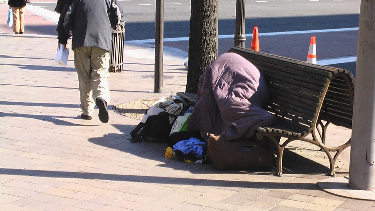 unhoused person laying on a bench