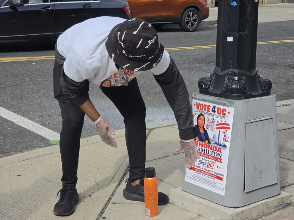 On Oct. 10, Rhonda Hamilton 4 DC volunteer, Juanita Briscoe, glues down a campaign poster on the corner of  7 and Monroe Streets Northeast. (Photo: Myla S. Roundy/HU News Service)